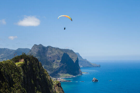 Overview of paraglider flying over Porto da Cruz village with Penha D'aguia mountain as background in Madeira island.