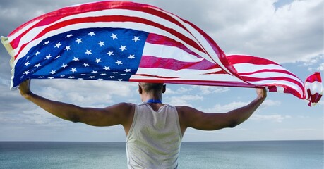 Composition of male athlete holding waving american flag against stormy sky and seaside