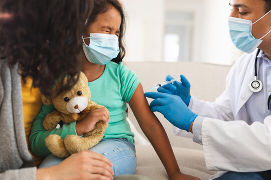 Hispanic Male Doctor Giving Covid Vaccination To Daughter Patient With Mother, Wearing Face Masks