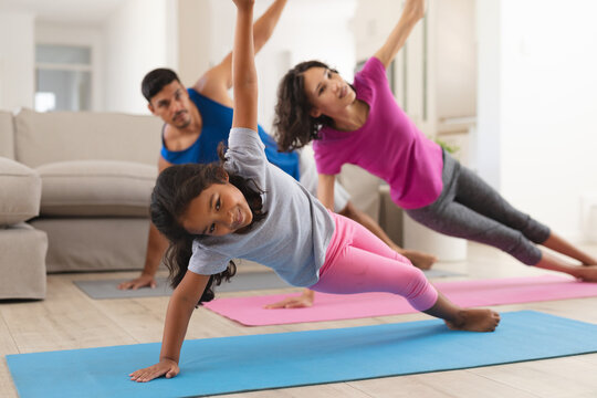 Smiling hispanic daughter and parents practicing yoga stretching in living room
