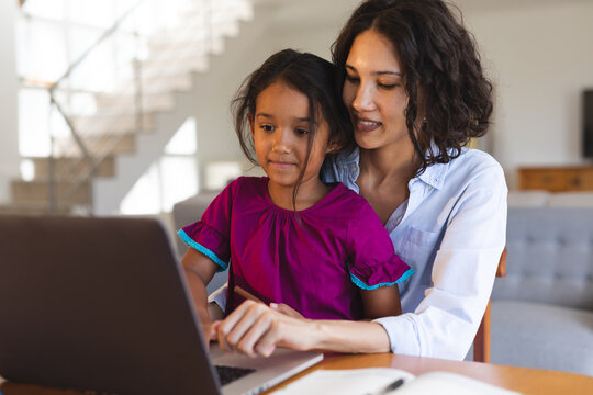 Smiling hispanic mother and daughter sitting in living room using laptop together