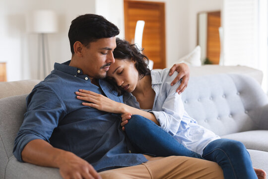Sad hispanic couple sitting on couch in living room embracing