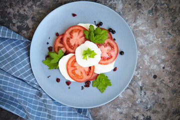 Italian caprese salad with sliced tomatoes, mozzarella, basil, olive oil on a blank plate. View from above.