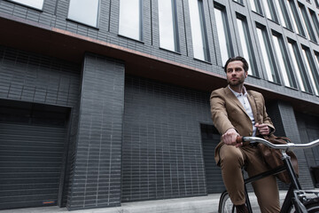 young businessman in suit with leather bag riding bicycle outside.