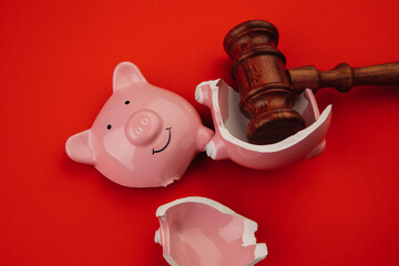 Broken pink piggy bank with wooden judge gavel on a red background close-up