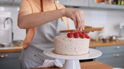 culinary, baking and cooking food concept - woman decorating raspberry cake with pistachio and on kitchen at home