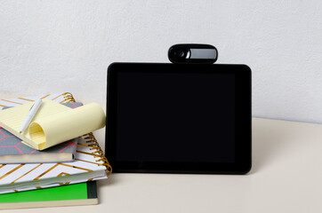 Blank screen of tablet, web camera, notebooks on the desk against bright wall.Empty space