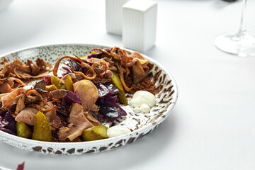 Thinly sliced beef tongue on a plate with fresh herbs and pickled cucumbers, close-up, light background
