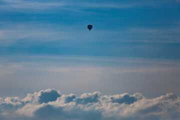 Small speck of hot air balloon floating contrasted against a blue sky with cumulus cloud landscape below. Travel, weather and climate concept.