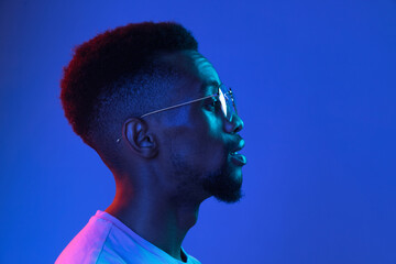 African-american young man's portrait on dark studio background in neon. Concept of human emotions,...