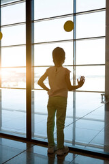 Fototapeta na wymiar girl with pigtail and medical mask leans her hand against window and looks at planes outside window of waiting room at airport