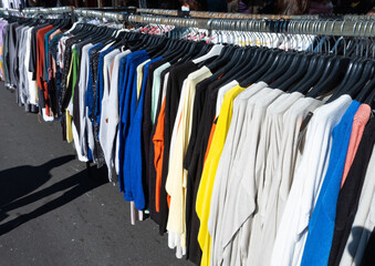 a lot of clothing hanging on hangers for sale at a local street market. flea market stall