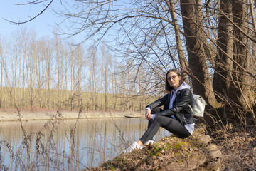 Naklejka na ściany i meble A girl is sitting on the river bank 