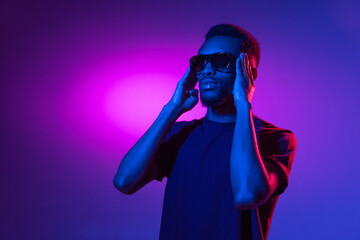African-american young man's portrait on dark studio background in neon. Concept of human emotions,...