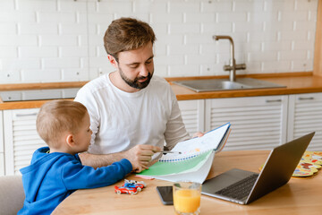 White father and son drawing and using laptop in kitchen at home