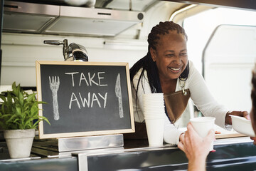African woman serving takeaway food with eco paper boxes inside food truck - Small business owners concept - Focus on face