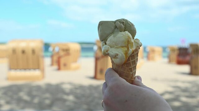 Slow motion 4K video of hand holding ice cream in cone waffle on a Baltic sea beach during summer sunny day
