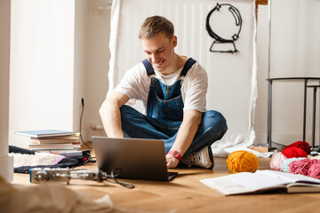 Young white man using laptop and sewing machine