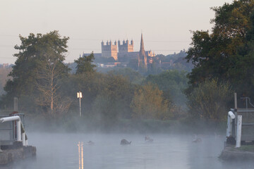 mist rising over the canal with lock gates, church and trees in the background