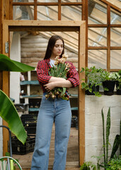 close-up portrait of a beautiful young Caucasian Brunette woman in a red shirt standing in a greenhouse holding a bouquet of wilted tulips