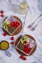 Lentil salad on a white background with blue, in square plates, with pieces of avocado, cherry tomato, onion and lemonade.