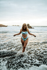 Fototapeta na wymiar Chica veraniega guapa en una playa de arena negra durante el atardecer luciendo su bikini de moda
