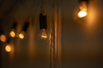 Round small bulbs glowing with warm orange light hang on a white wall. Loft-style decor. The bulbs are connected to each other like a garland. Close-up