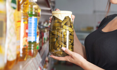 Woman holding jar of canned cucumbers at supermarket.