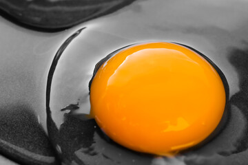 One bright round yolk in raw whites, uncooked small fried eggs is a simple breakfast in a black skillet. Close-up, macro