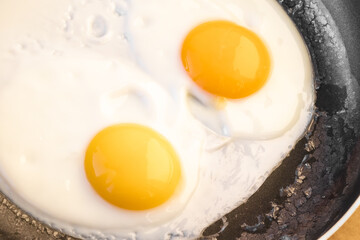 Two bright round raw yolks in whites with edge cracks in a frying pan. Cooked tender, soft fried eggs is a simple dish. Top view