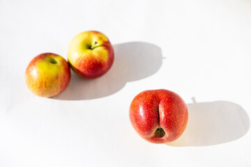 Bright ripe red apple of an unusual shape in the shape of an ass in the light of the sun on a white background with two usual apples with long shadows. Close-up