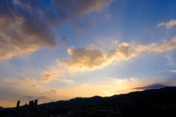 タイトル : 日の入り前の六甲山。西の空と雲がオレンジ色に染まるマジックアワー。高層ビルがシルエットで浮かぶ。1日の終わり。