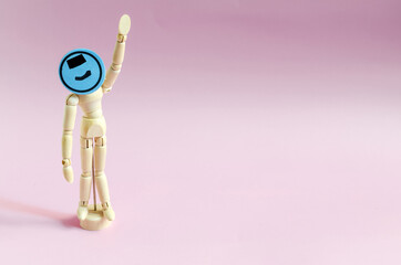 A figure of a wooden man with a raised hand and a blue painted smiley face. Figure of a wooden man on a pink background of kopi space