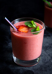 Strawberry smoothie in a glass with mint leaves, strawberry slices and a metal tube shot in a low key