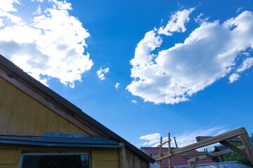 Fototapeta premium Against the background of a timber frame building, a blue sky with white clouds on a bright sunny summer day. Rural landscape.