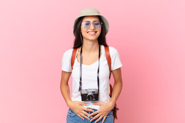 pretty hispanic tourist laughing out loud at some hilarious joke with a photo camera and a hat