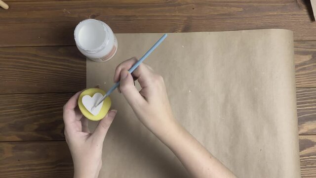 Woman applies acrylic paint with brush to potato stamp in form of heart to do print on craft paper. Hands decorate wrapping paper for Valentine's day on wooden table. Diy and handmade on quarantine.