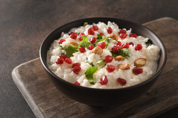 Curd Rice with pomegranate, cilantro, mustard seeds, ginger on a brown background. Close up.