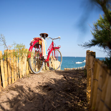 Vieux vélo rouge au soleil en bord de mer, vu sur la plage en été.