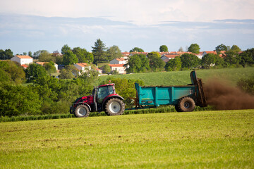 Obraz premium Tracteur pratiquant de l'épandage en campagne devant un village en France.