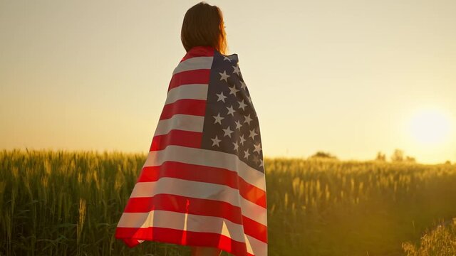 Silhouette girl holding American stars and stripes flag, standing in summer sunshine