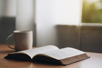 Open bible with a cup of coffee for morning devotion on wooden table with window light.book and...