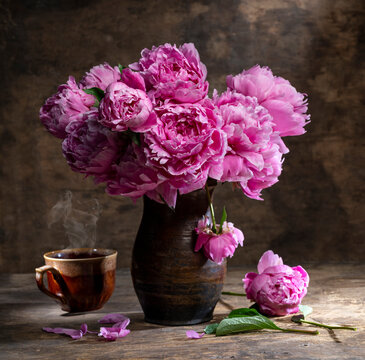 Beautiful bouquet of pink peonies in vase and cup of hot tea