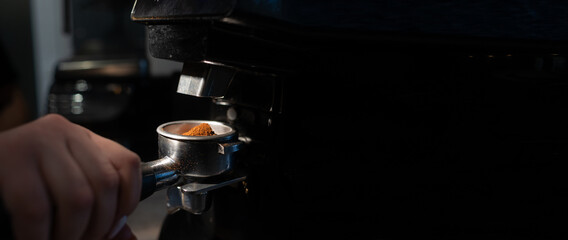 close-up of a barista holding a portafilter with coffee in front of an electric coffee grinder in a...