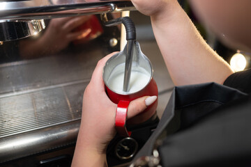 Close-up of a barista whipping milk in a coffee machine and preparing a morning latte in a cafe. Cappuccino and milk whipped with a steam wand or cappuccino maker.