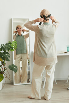 Full Length Back View At Mature Woman Putting On Headscarf By Mirror And Getting Ready To Go Out