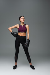 Fototapeta na wymiar confident sportswoman in boxing gloves standing with hand on hip on grey background.