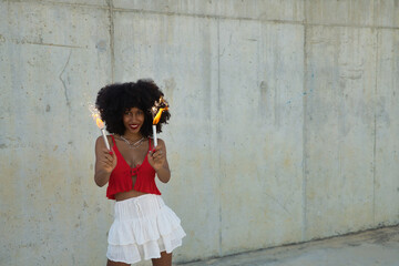 Young, beautiful African-American woman having fun and playing with sparklers on a gray cement background.