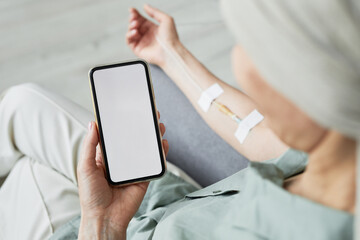 Minimal close up of unrecognizable woman getting IV drip and using smartphone with blank screen, copy space