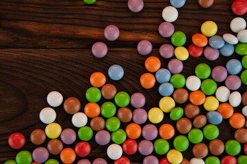 background in the form of small round colored candies sprinkled on a wooden background